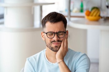 Woman holding her cheek while sitting in dental chair