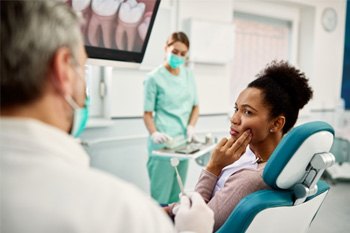 woman looking at dentist holding her cheek in pain